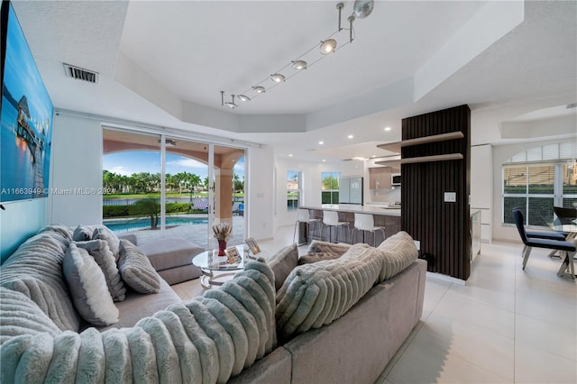 living room featuring light tile patterned flooring, a tray ceiling, and a wealth of natural light