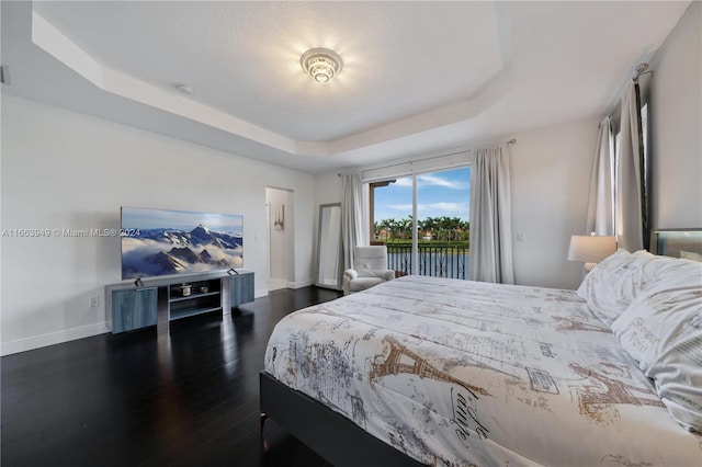 bedroom with a raised ceiling, dark hardwood / wood-style floors, and access to exterior