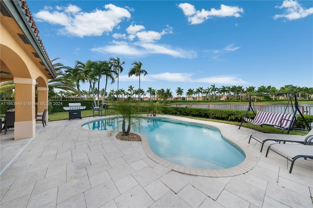 view of swimming pool with grilling area, a water view, and a patio area