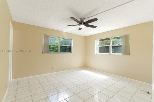 tiled empty room featuring a textured ceiling, a healthy amount of sunlight, and ceiling fan