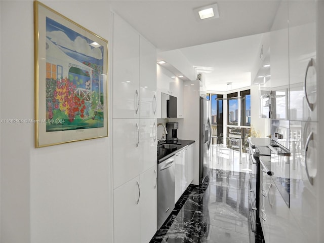 kitchen with appliances with stainless steel finishes, a wall of windows, white cabinetry, and sink