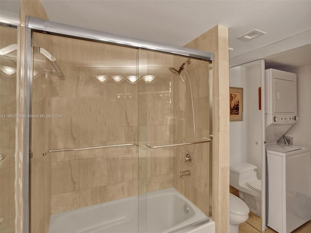 bathroom featuring stacked washer / dryer, shower / bath combination with glass door, toilet, and tile patterned floors