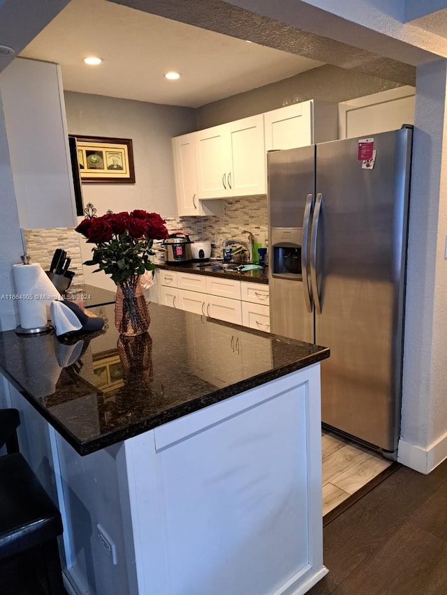 kitchen featuring dark stone counters, wood-type flooring, tasteful backsplash, stainless steel refrigerator with ice dispenser, and white cabinetry