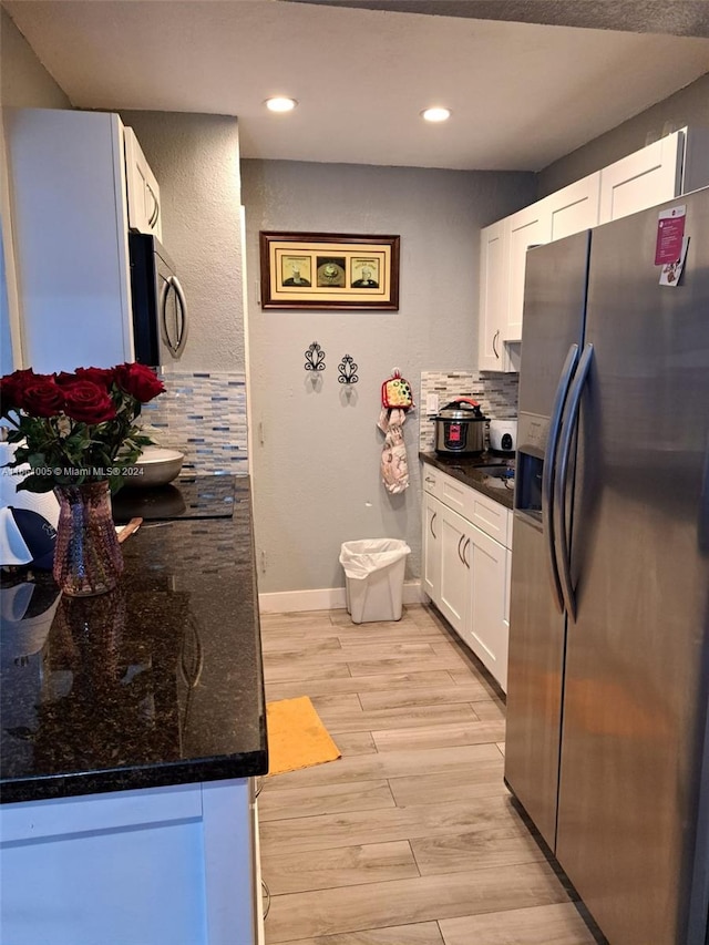 kitchen with dark stone counters, white cabinets, light hardwood / wood-style flooring, backsplash, and appliances with stainless steel finishes