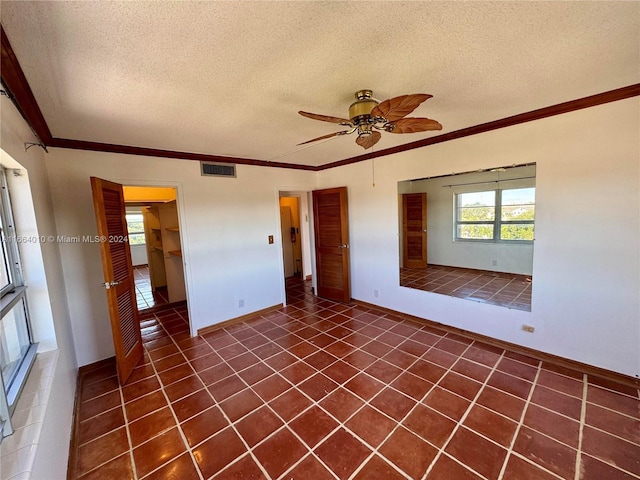 empty room featuring dark tile patterned flooring, ceiling fan, ornamental molding, and a textured ceiling