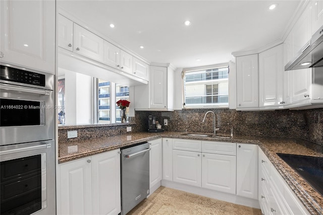 kitchen with appliances with stainless steel finishes, wall chimney range hood, white cabinetry, and decorative backsplash