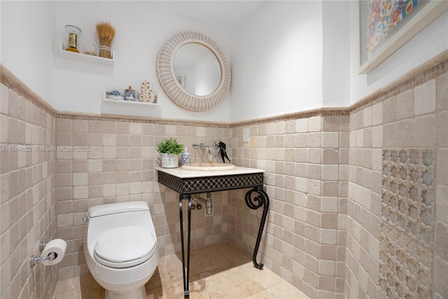 half bathroom featuring wainscoting, a sink, toilet, and tile walls