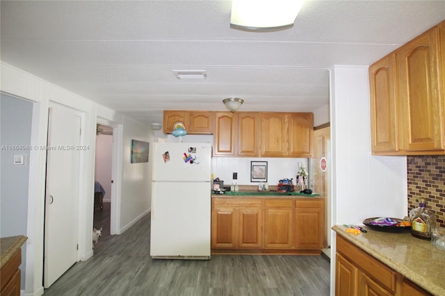 kitchen with light stone countertops, backsplash, hardwood / wood-style floors, and white refrigerator