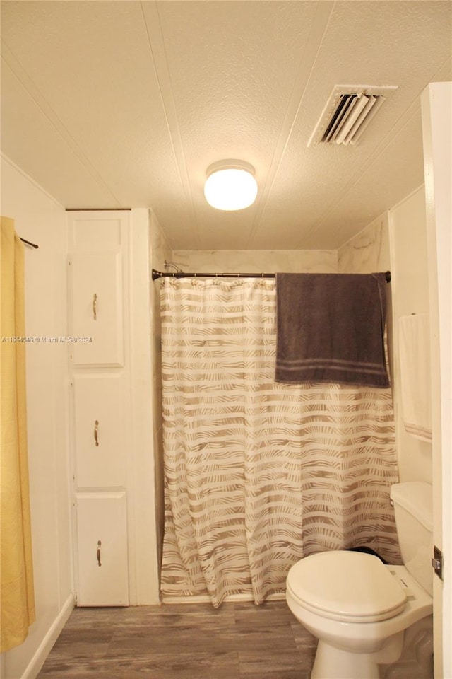 bathroom with curtained shower, a textured ceiling, toilet, and hardwood / wood-style flooring