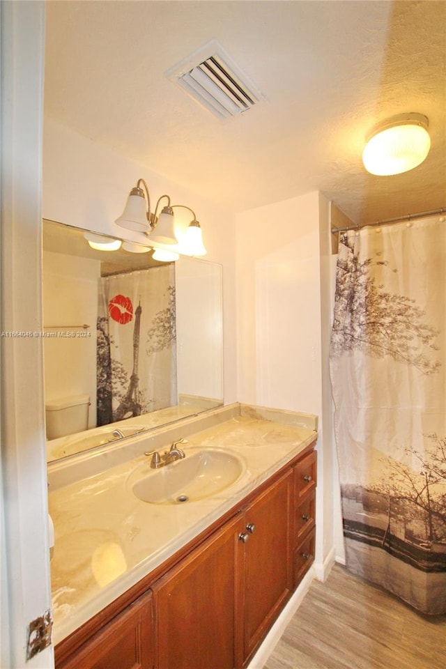 bathroom with a shower with shower curtain, hardwood / wood-style flooring, vanity, and toilet