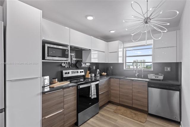 kitchen featuring appliances with stainless steel finishes, light hardwood / wood-style floors, white cabinets, an inviting chandelier, and sink