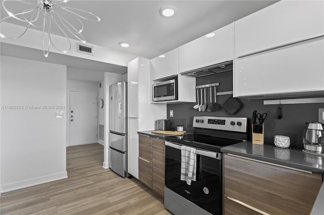 kitchen with ventilation hood, a notable chandelier, white cabinets, light hardwood / wood-style flooring, and appliances with stainless steel finishes