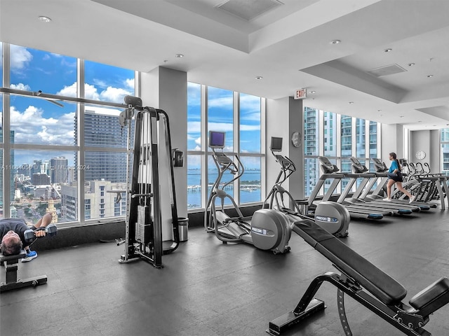 exercise room featuring floor to ceiling windows, a water view, and a tray ceiling