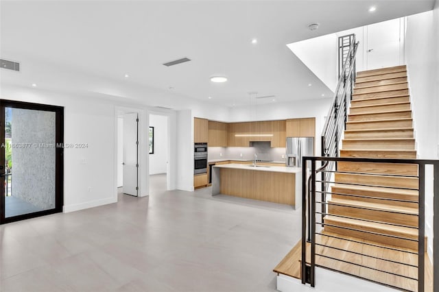 kitchen with stainless steel appliances, light brown cabinets, a kitchen island with sink, and sink