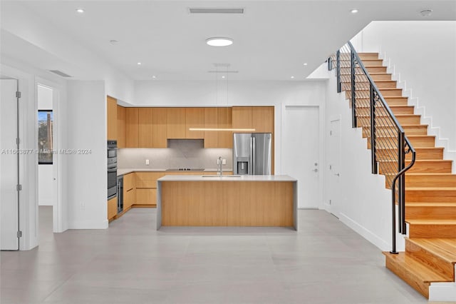 kitchen with an island with sink, sink, stainless steel appliances, light brown cabinetry, and decorative backsplash