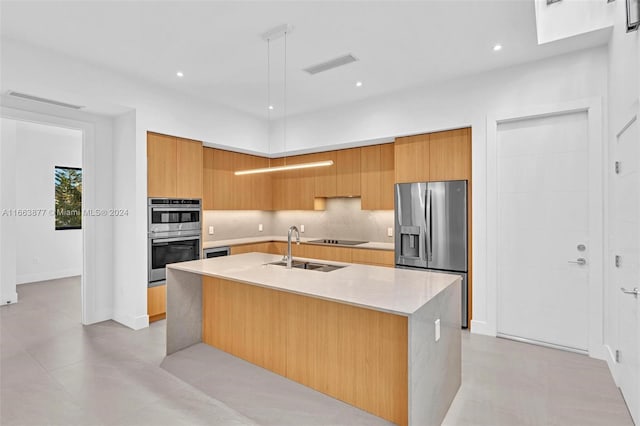 kitchen featuring sink, a center island with sink, stainless steel appliances, light stone countertops, and decorative backsplash