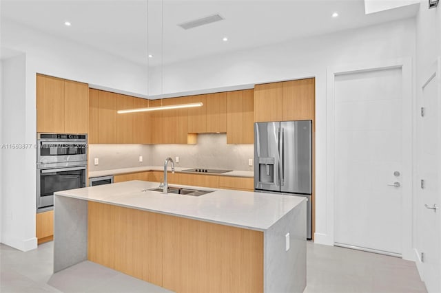 kitchen featuring appliances with stainless steel finishes, decorative backsplash, an island with sink, light stone counters, and sink