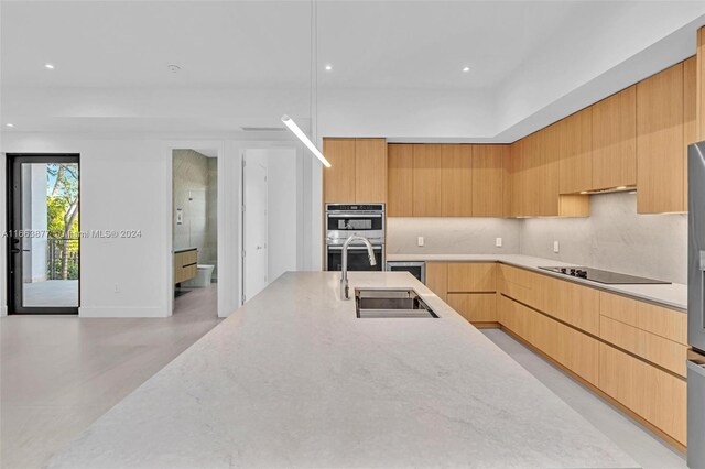 kitchen with sink, double oven, black electric cooktop, light brown cabinetry, and decorative backsplash