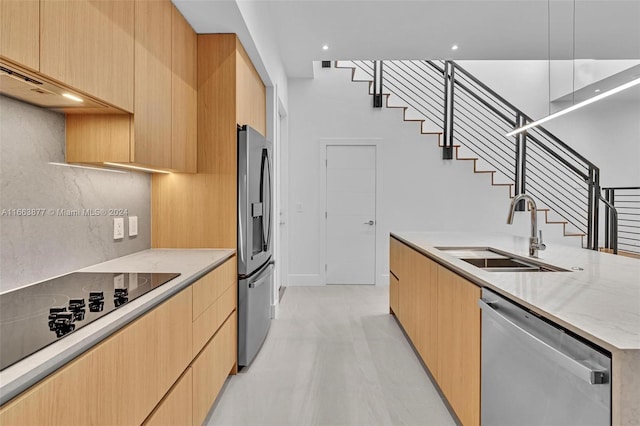 kitchen with appliances with stainless steel finishes, light stone counters, light wood-type flooring, light brown cabinetry, and sink