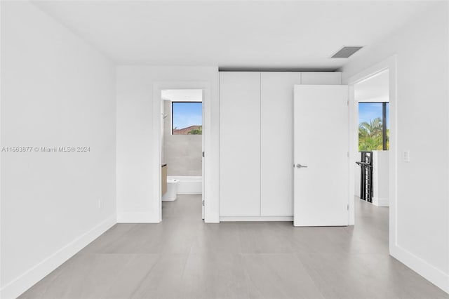 unfurnished bedroom featuring connected bathroom, multiple windows, and light tile patterned flooring