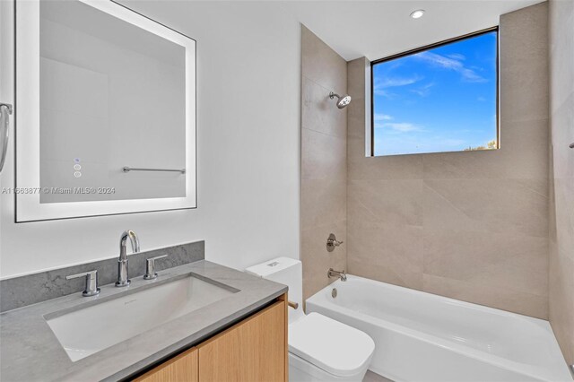 full bathroom featuring tiled shower / bath, vanity, and toilet