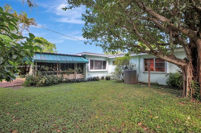 rear view of house with a lawn, a sunroom, and central AC unit