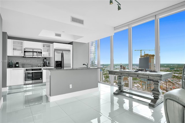 kitchen featuring white cabinets, expansive windows, light tile patterned floors, appliances with stainless steel finishes, and stone countertops