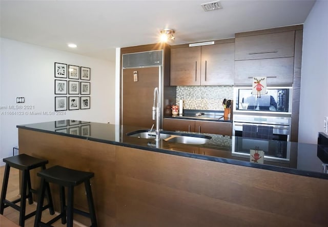 kitchen with backsplash, built in appliances, wood-type flooring, a kitchen bar, and sink