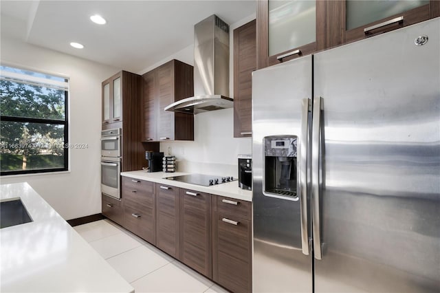 kitchen with dark brown cabinets, light tile patterned flooring, appliances with stainless steel finishes, and wall chimney range hood