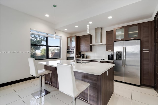 kitchen featuring sink, wall chimney range hood, a kitchen breakfast bar, appliances with stainless steel finishes, and decorative light fixtures