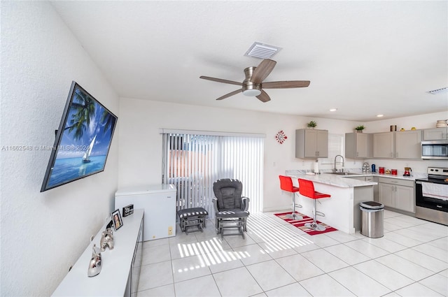 kitchen with ceiling fan, gray cabinetry, a kitchen island, appliances with stainless steel finishes, and a kitchen breakfast bar