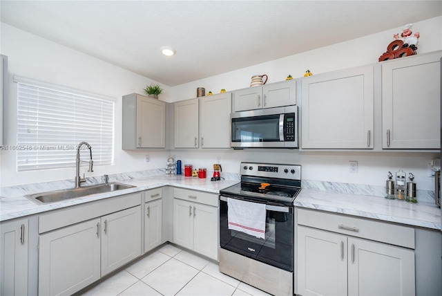 kitchen with light tile patterned floors, sink, gray cabinets, stainless steel appliances, and light stone countertops