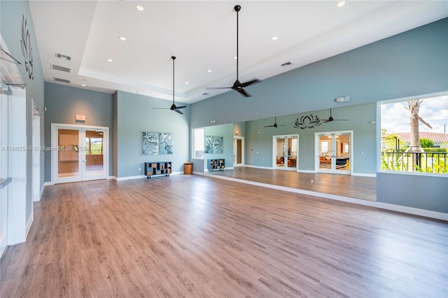 unfurnished living room with a raised ceiling, light wood-type flooring, a high ceiling, ceiling fan, and french doors