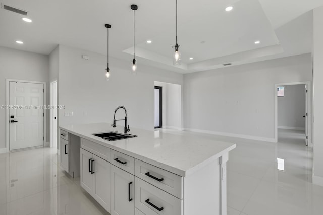 kitchen featuring white cabinets, pendant lighting, sink, a kitchen island with sink, and a tray ceiling