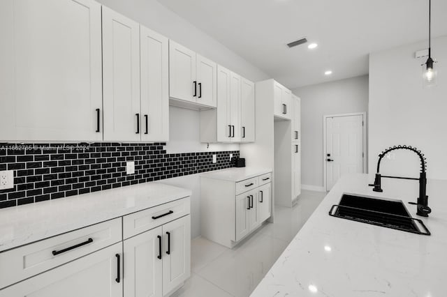 kitchen with light stone countertops, white cabinets, sink, and decorative light fixtures