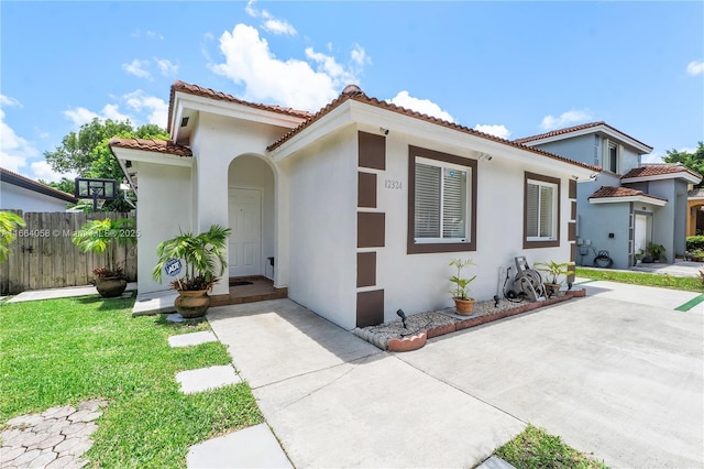 mediterranean / spanish house with a tiled roof, a front yard, fence, and stucco siding