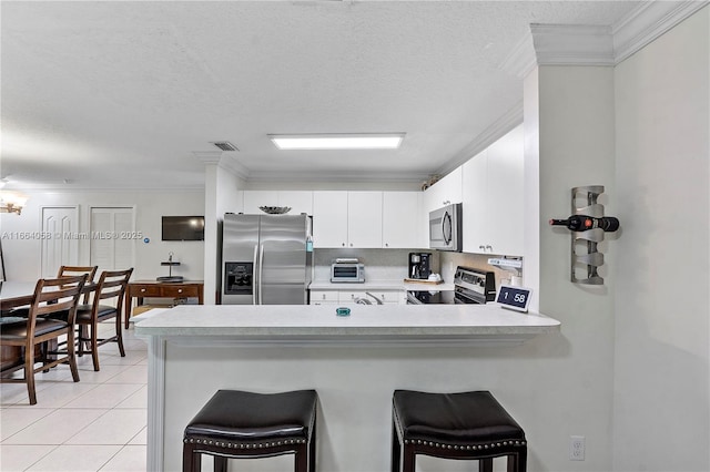 kitchen with light tile patterned flooring, a peninsula, light countertops, appliances with stainless steel finishes, and a kitchen bar