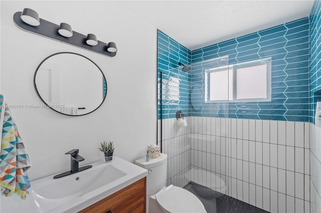 bathroom with a tile shower, vanity, and toilet