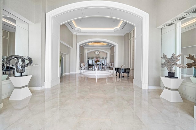 hall featuring ornamental molding, arched walkways, marble finish floor, and a tray ceiling