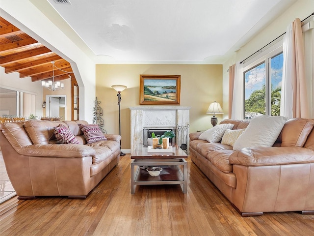 living room with a notable chandelier, a premium fireplace, beamed ceiling, and light wood-type flooring