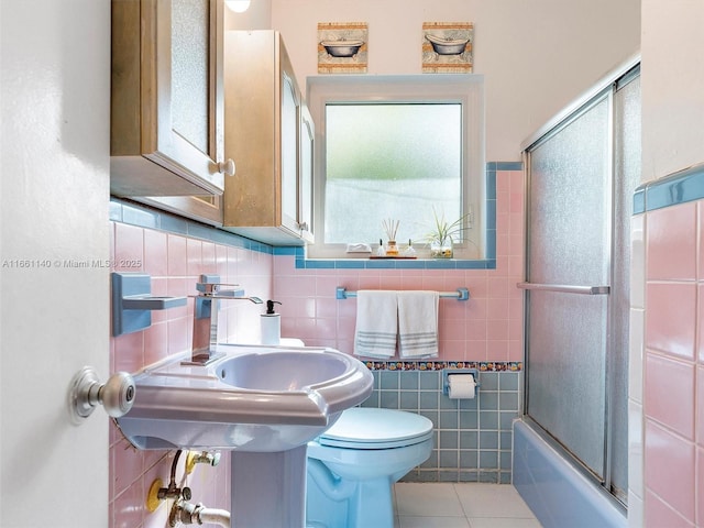 full bathroom featuring toilet, sink, combined bath / shower with glass door, tile walls, and tile patterned flooring