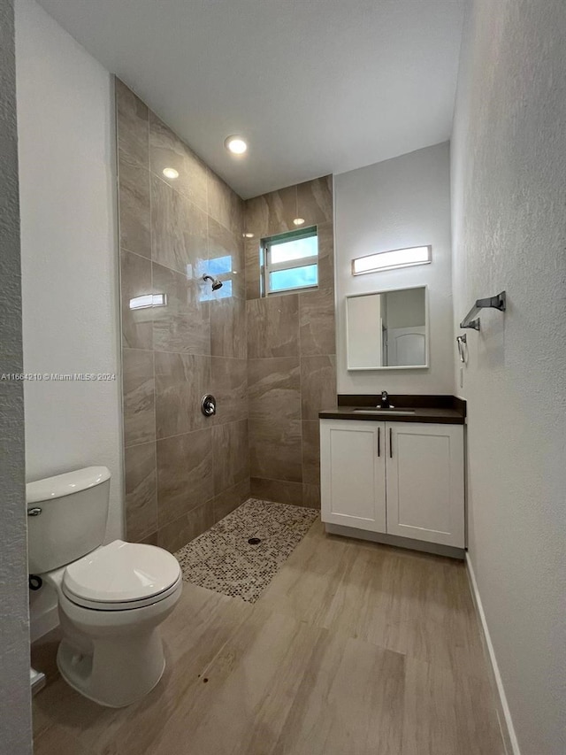 bathroom with a tile shower, vanity, hardwood / wood-style floors, and toilet