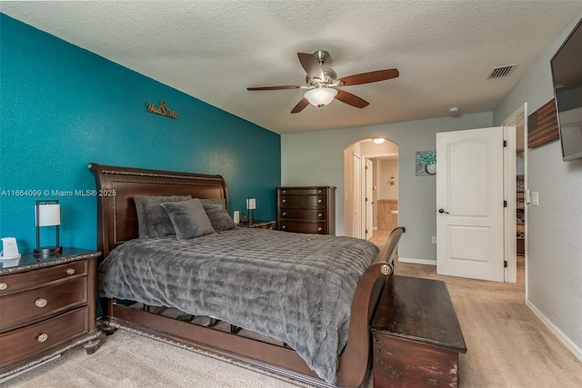 bedroom featuring ceiling fan, ensuite bathroom, light carpet, and a textured ceiling