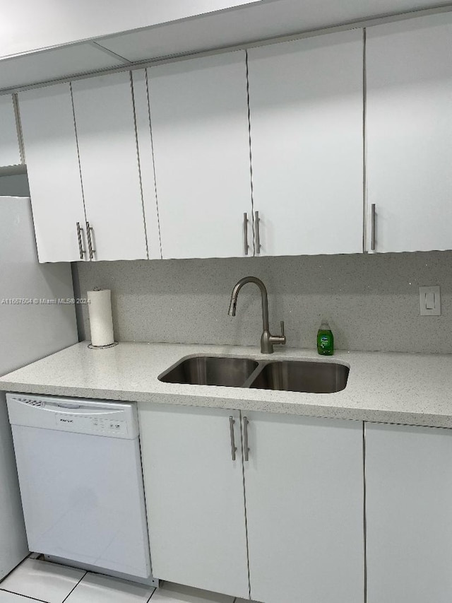kitchen with light stone counters, white cabinets, white dishwasher, and a sink