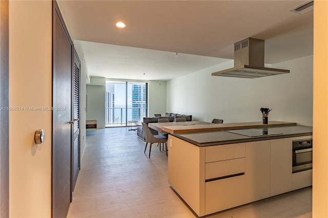 kitchen featuring floor to ceiling windows, island range hood, oven, light hardwood / wood-style flooring, and black electric stovetop