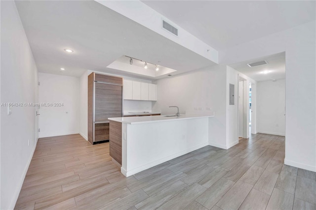 kitchen with white cabinets, sink, kitchen peninsula, built in fridge, and light wood-type flooring