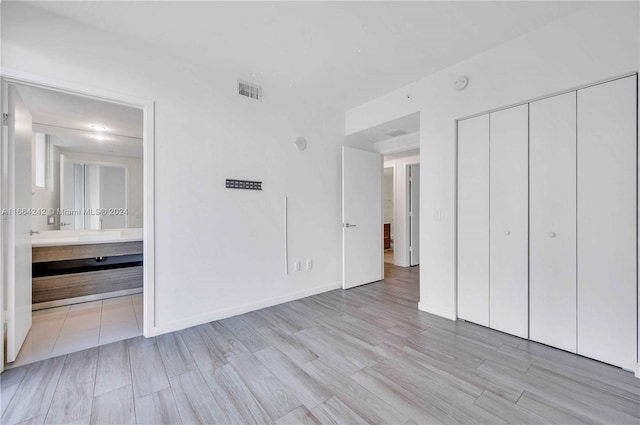 unfurnished bedroom with light hardwood / wood-style flooring, ensuite bath, and a closet