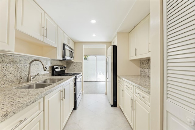 kitchen with tasteful backsplash, stainless steel appliances, light stone countertops, sink, and white cabinets