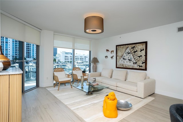 living room with wood finished floors, visible vents, baseboards, a view of city, and a wall of windows