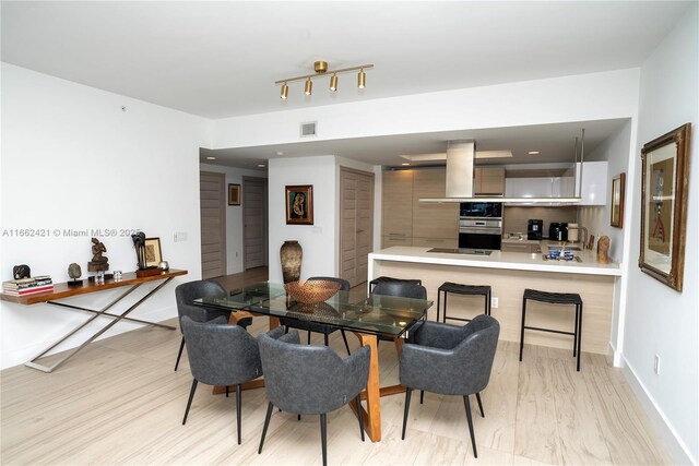 kitchen featuring black electric stovetop, track lighting, kitchen peninsula, island exhaust hood, and light brown cabinetry